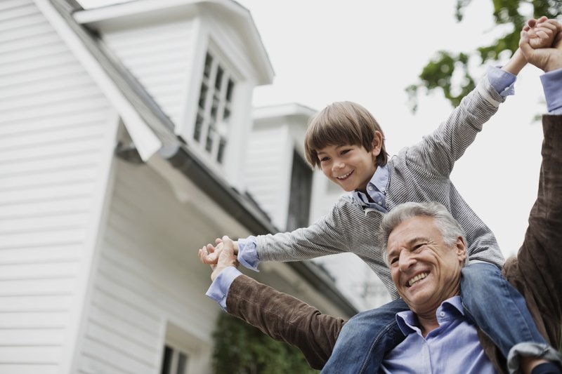 A grandfather giving his grandson a piggyback ride in front of their home